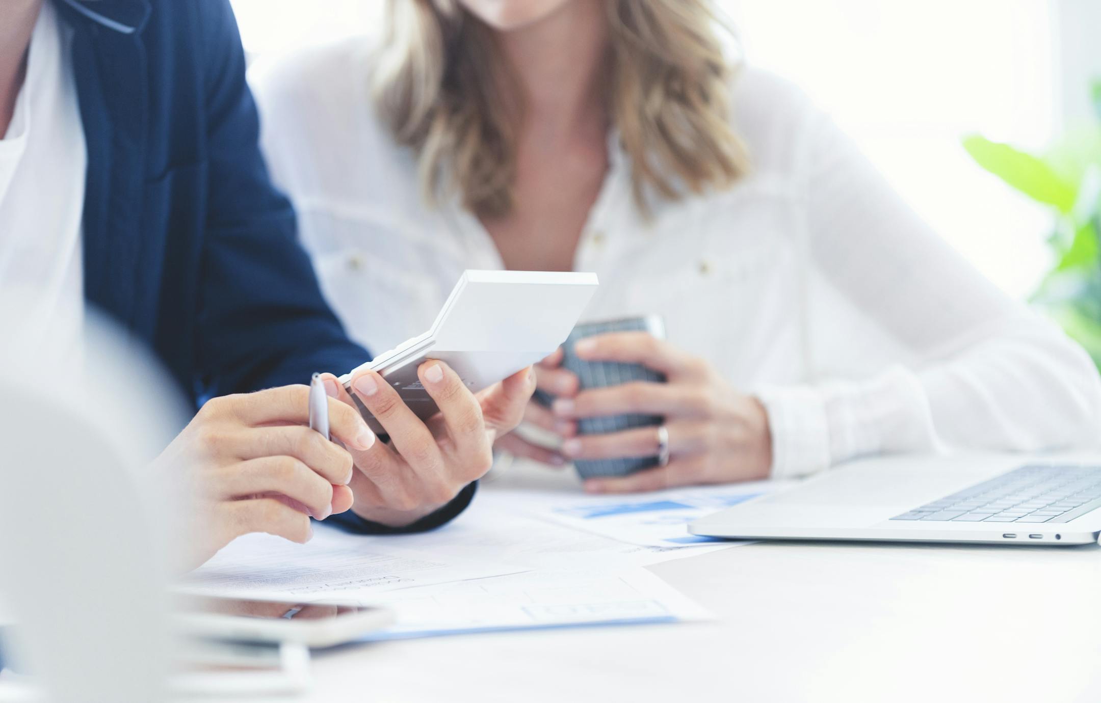 Young Couple working on their home finances. They are working at the dining room table using a calculator. There is some paperwork on the table. Close up tight crop.