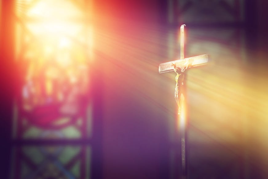 Crucifix, Jesus on the cross in church with ray of light from stained glass.
