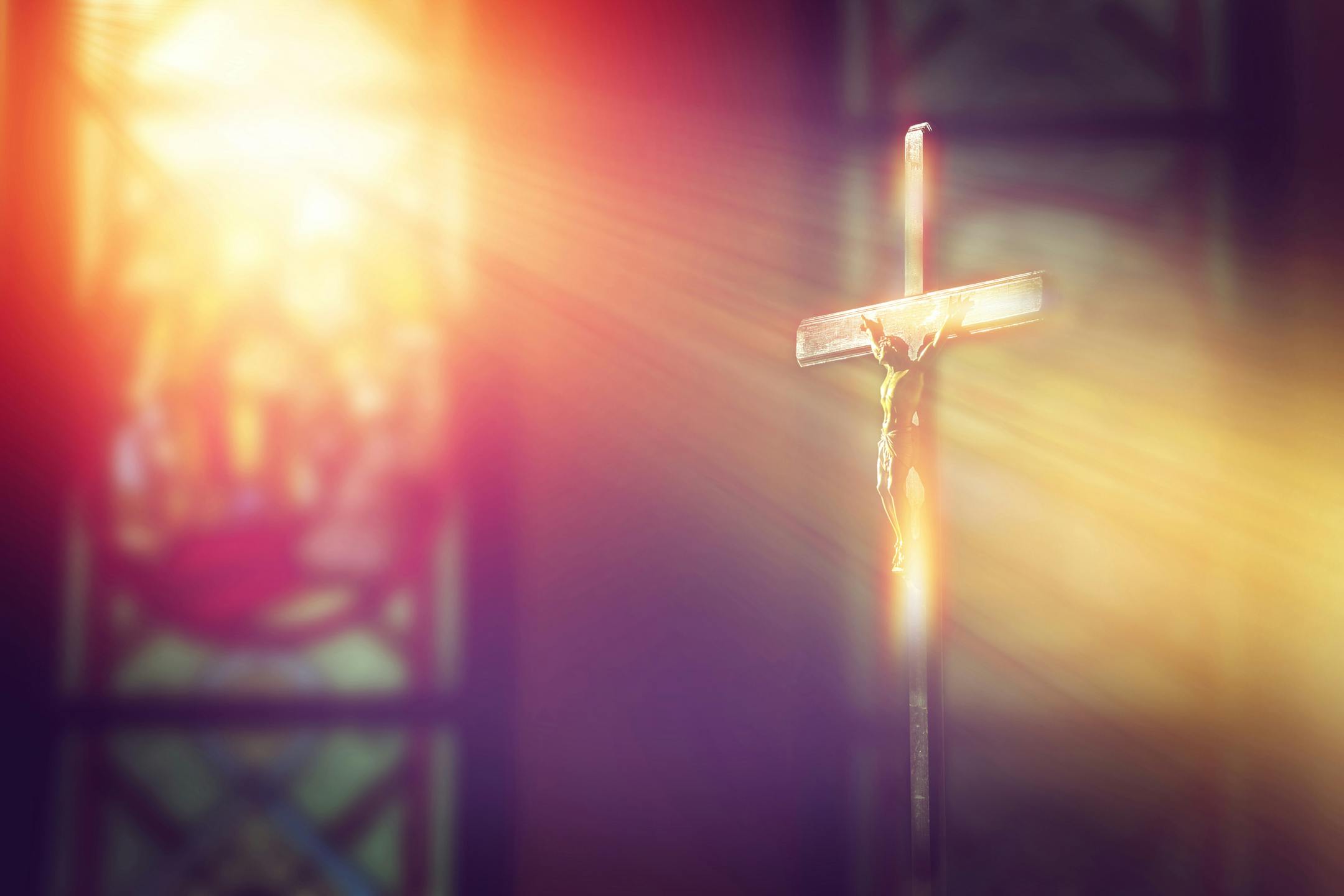 Crucifix, Jesus on the cross in church with ray of light from stained glass.