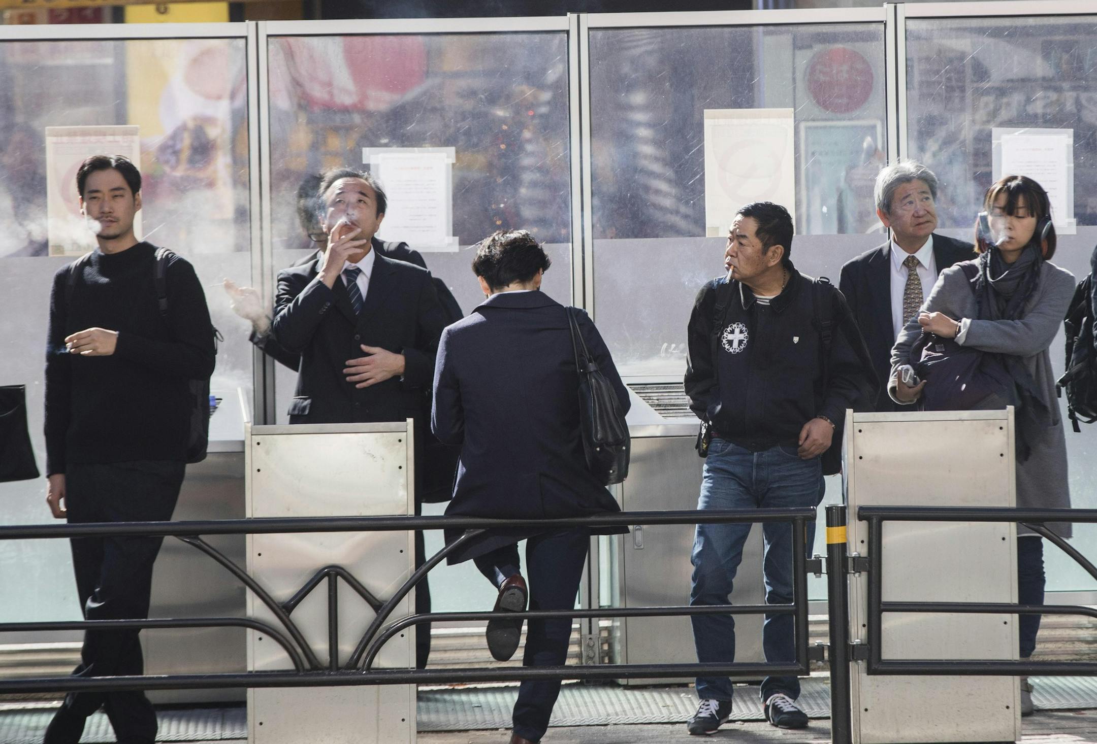 People smoke cigarettes in a smoking section on the street in the Shibuya district of Tokyo on Nov. 16, 2017. MUST CREDIT: Bloomberg photo by Keith Bedford.