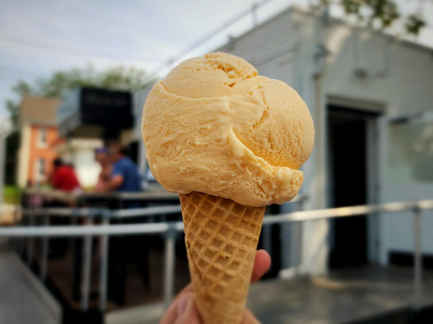 Sugar cone with a light orange scoop of melon ice cream, held up in front of Dream Creamery