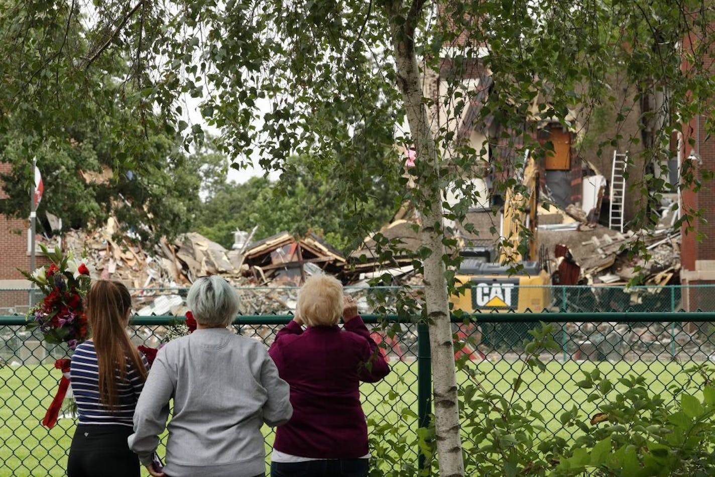 Three women stood near a makeshift memorial outside the fenced-off collapsed building at Minnehaha Academy's Upper School campus on Thursday.